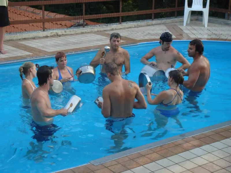 Pino Poclen e un gruppo di persone in piscina suonano tamburi e percussioni nell’acqua