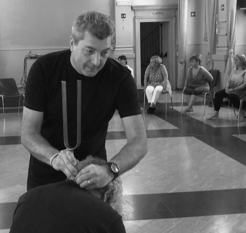 Pino Poclen appoggia un grande diapason sulla testa di una persona durante una seduta